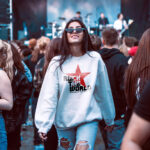 Model wearing Raverge 'Rock the World' women's white sweatshirt with bold lettering and red star graphic.