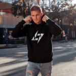Model wearing Raverge men's black hoodie with the brand logo, showcasing sleek streetwear style.