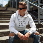 Model wearing Raverge men's white hoodie Deny Ordinary bold slogan confident streetwear look