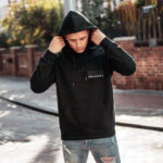 Model wearing Raverge Escape Velocity men's black hoodie with sci-fi title graphic.