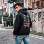 Model wearing Raverge Bushido men's black hoodie with samurai-themed graphic on the back.