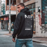 Model wearing Raverge Next Generation men's black hoodie with sci-fi graphic on the back.