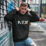Model wearing Raverge Next Generation men's black hoodie with 'NEXT' title.