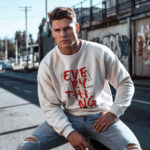 Model wearing men's white Challenge Everything sweatshirt with bold graphic text