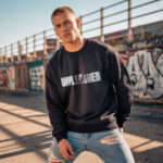 Model wearing the men's Unleashed black sweatshirt with bold "Unleashed" text sliced by red claw marks.
