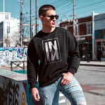 Model wearing men's IN sweatshirt with mirrored geometric typography design on black fabric