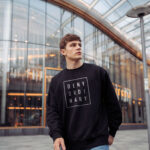 Model wearing men's Deny Ordinary black sweatshirt with bold Raverge slogan