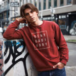 Model wearing men's Deny Ordinary red sweatshirt with bold Raverge slogan