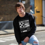 Man wearing Raverge men's Caution black sweatshirt featuring futuristic sci-fi graphics.