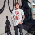 White 'Challenge Everything' t-shirt with bold typography, streetwear style worn by a model.