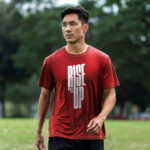 Model wearing the red Rise Up T-shirt with bold "Rise Up" typography and "No matter what" text beside it. A statement t-shirt for those who never back down.