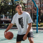Model wearing the white Rise Up T-shirt with bold "Rise Up" typography and "No matter what" text beside it. A statement t-shirt for those who never back down.