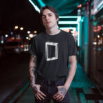 Model wearing a black "Nexus" t-shirt with a futuristic intertwined rectangular graphic, representing a sci-fi aesthetic.