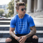 Male model showcasing blue Raverge's 'Deny Ordinary' t-shirt in casual streetwear outfit