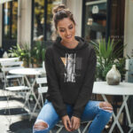 Model wearing Raverge women's black hoodie with the 'Divine Grace' statue and geometric design.
