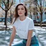 Model wearing white Raverge Embrace Harmony Women's T-Shirt in white with elegant script typography.
