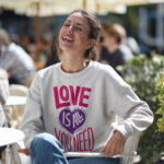 Model wearing Raverge Love is All You Need white sweatshirt - Positive Message Women's Fashion