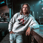 Model wearing Raverge men's white hoodie with "Rock the World" red star design.