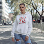 Model wearing Raverge women's white hoodie with "Be Iconic" design.