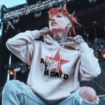 Model wearing Raverge women's white hoodie with "Rock the World" design and bold red star for rock music lovers.