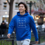 Model wearing Raverge men's blue hoodie Deny Ordinary bold slogan confident streetwear look