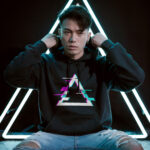 Model wearing Raverge Apex men's black hoodie with glitched triangle graphic for gamers and sci-fi fans.