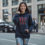 Model wearing Raverge women's navy hoodie with "Be Iconic" design.